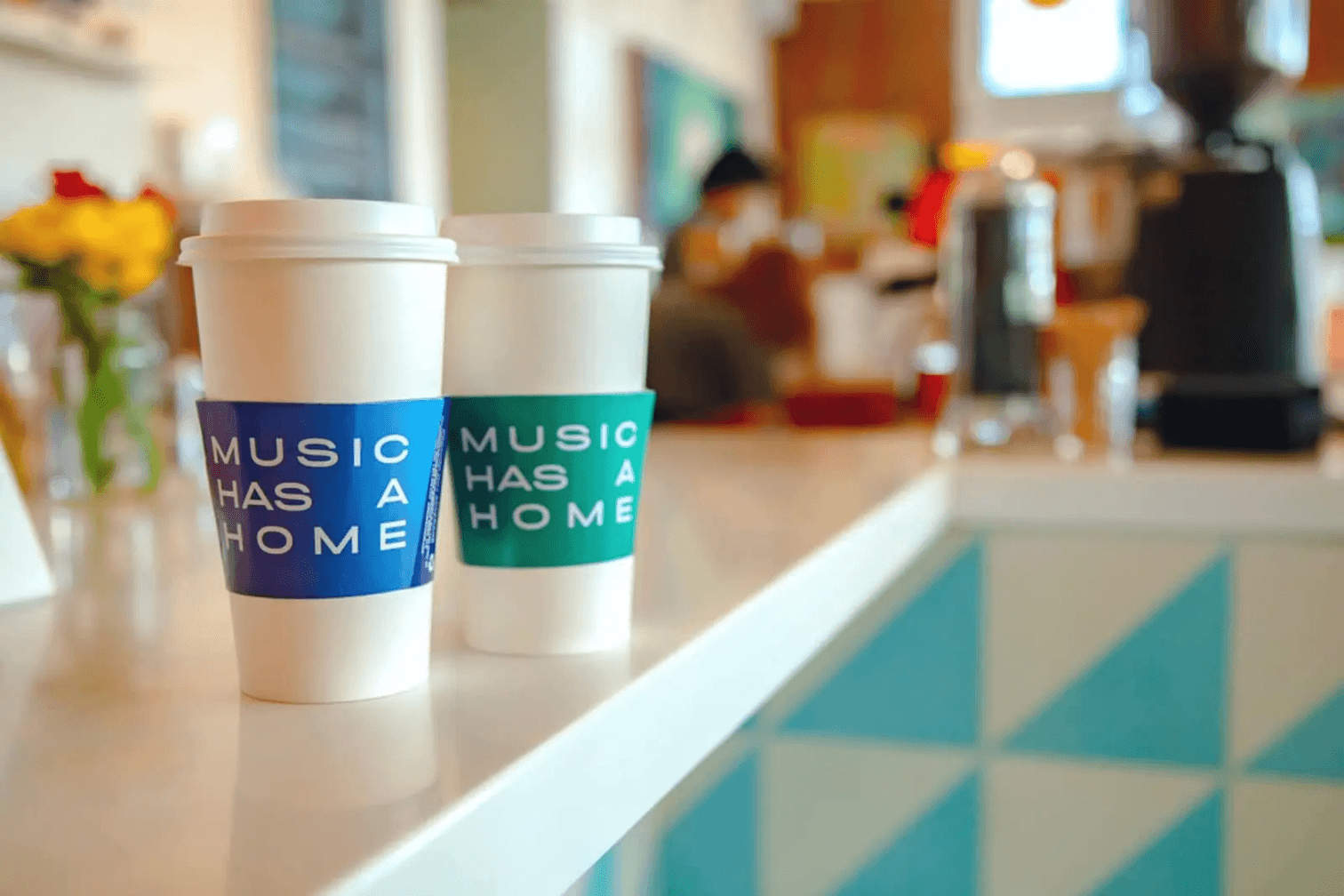 Two coffee cups with branded coffee sleeves on them sat on a countertop of a coffee shop.