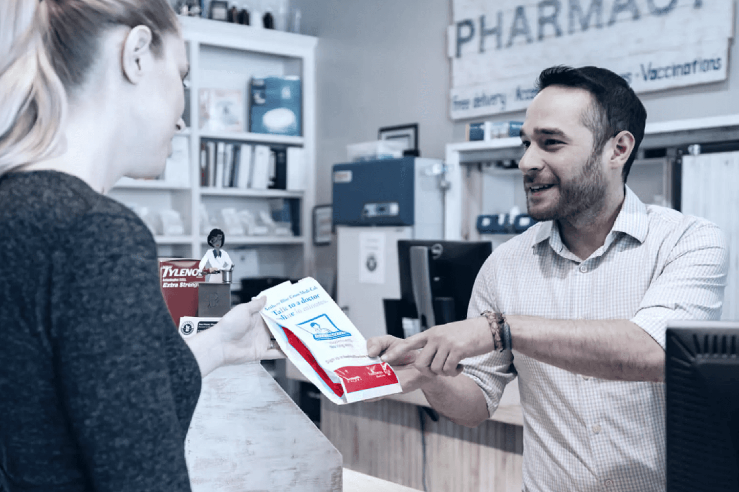 Pharmacist handing a prescription bag to a patient, pointing out information on the bag.