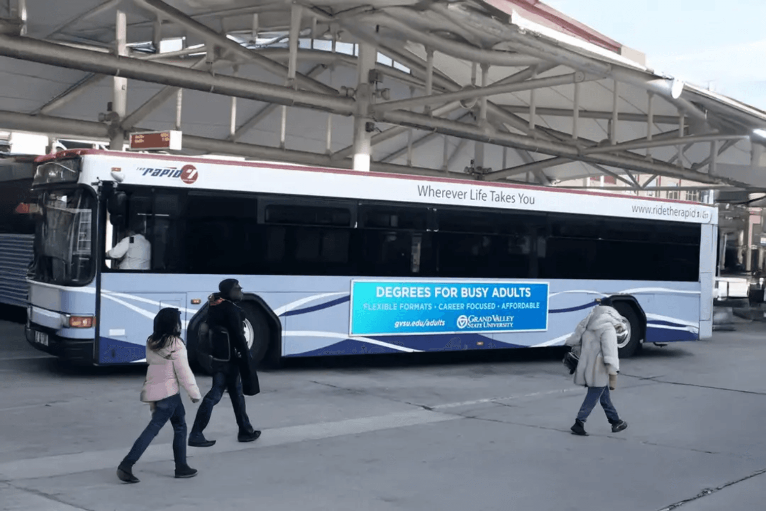Passengers boarding a fixed route bus with branded advertisements on the side and back of the bus.